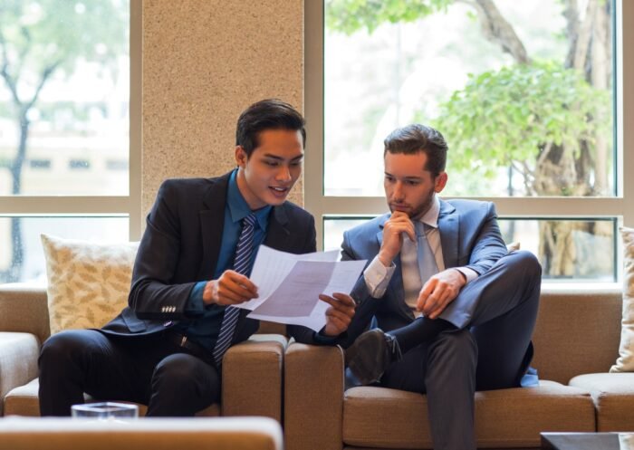 two-business-men-discussing-document-lounge (1) Business professionals reviewing contract documents