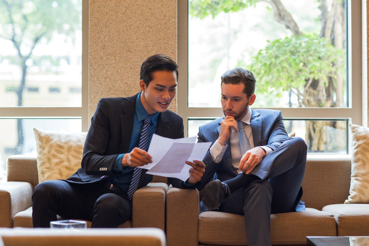 two-business-men-discussing-document-lounge (1) Business professionals reviewing contract documents